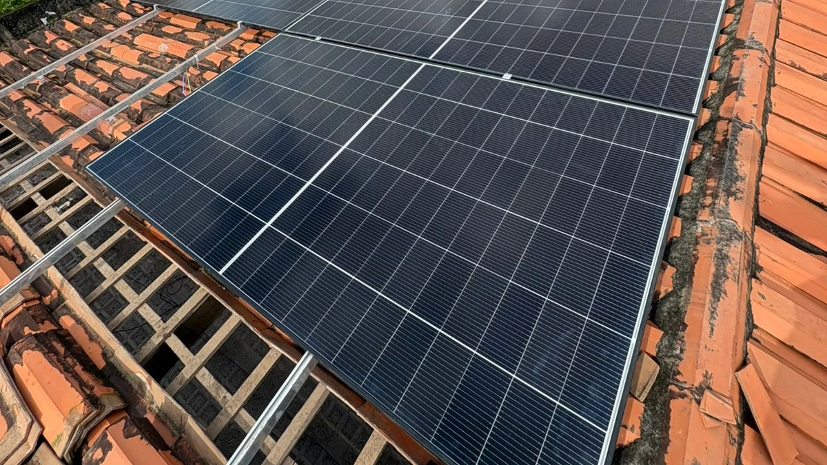 Painéis fotovoltaicos instalados sobre telhado cerâmico, vistos de perto com estrutura metálica aparente.