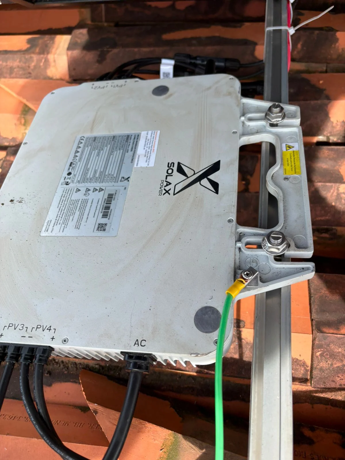 Equipamento de conversão instalado sob painel solar, com cabos e estrutura de fixação visíveis.
